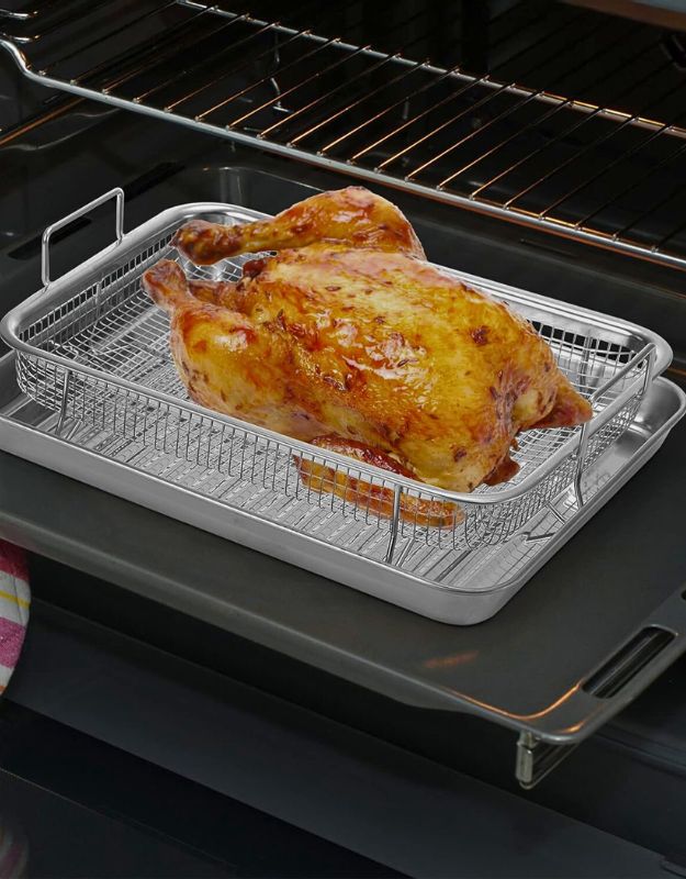 Whole roasted chicken in stainless steel air fryer basket and tray set inside an oven